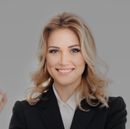 Smiling blonde woman in a black blazer against a light gray background