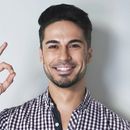 Smiling man in a checkered shirt waving against a plain gray background
